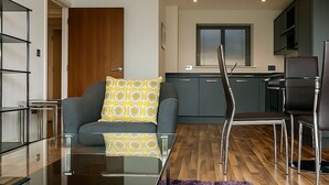 A modern living room with a glass coffee table, a sofa with patterned cushions, and a purple rug.