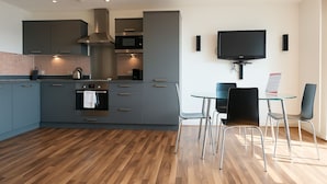 A modern kitchen with grey cabinets, a stainless steel range hood, a microwave, and a built-in oven. There is a dining area with a glass table and black chairs.