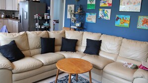 Uma sala de estar com um sofá seccional bege, uma mesa de centro de madeira e um tapete com padrão azul e branco.