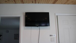 Quarto com televisão de tela plana fixada na parede, porta branca e placa de proibido fumar.