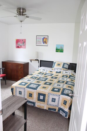 Un dormitorio con cama, cómoda de madera, escritorio y ventilador de techo.