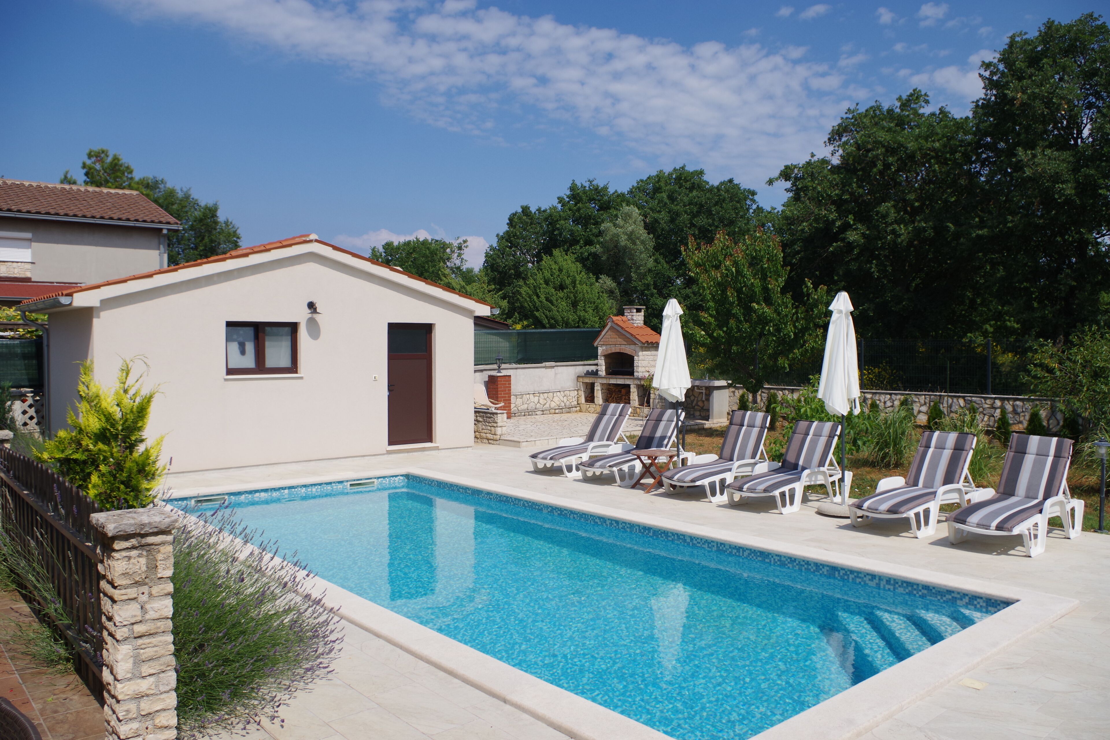 Ein rechteckiger Pool mit Liegestühlen und Sonnenschirmen, umgeben von einer Steinmauer und Pflanzen.