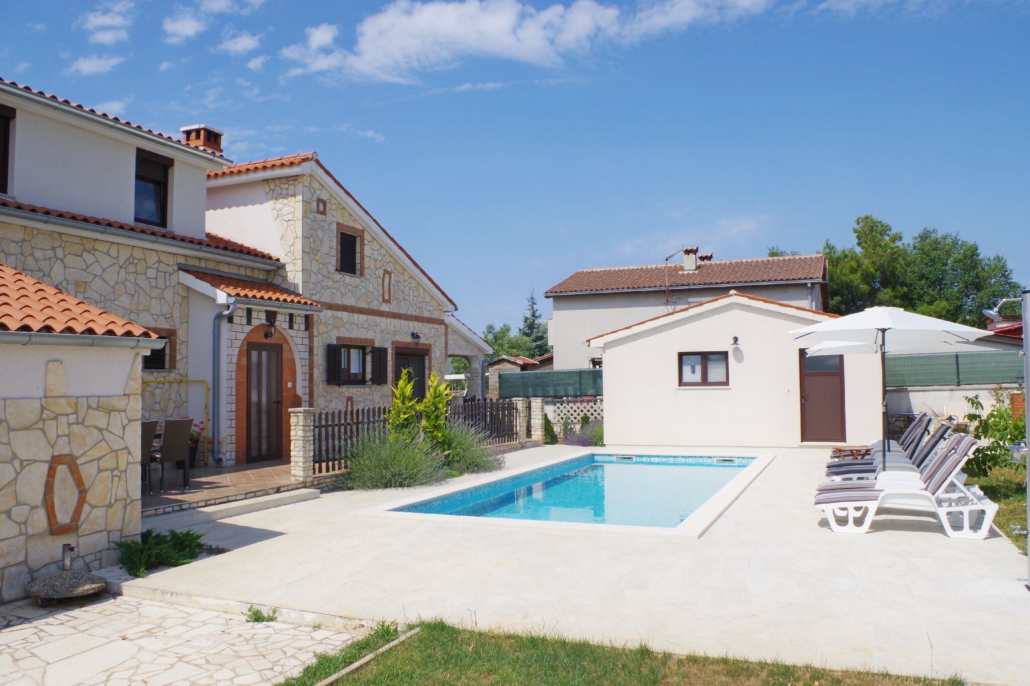 A residential property with a swimming pool, stone and tiled exterior, and a fenced garden area.