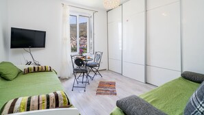 A modern hotel room with a large bed, a TV, a balcony with a view, and a dining area. - Apartment Luka (Dubrovnik)