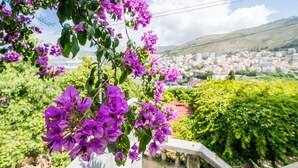 A balcony with purple bougainvillea flowers, a cityscape in the background, and a clear sky. - Apartment Luka (Dubrovnik)