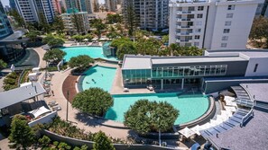 An aerial view of a hotel with a large swimming pool, surrounded by lush greenery and modern buildings.