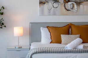 Un lit bien fait, avec une tête de lit grise, des oreillers blancs et à motifs, et une couverture grise.