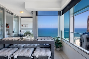 A balcony with a view of the ocean, a wicker sofa with striped cushions, and a small table with a plant. - Luxury 3 Bedroom Apartment with Ocean Views (Surfers Paradise)