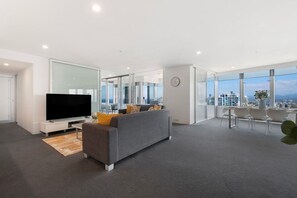 A modern living room with a flat-screen TV, grey sofa, and a dining area with chairs and a table. - Luxury 3 Bedroom Apartment with Ocean Views (Surfers Paradise)
