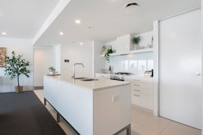 A modern kitchen with a central island, built-in appliances, and a view to the living area. - Luxury 3 Bedroom Apartment with Ocean Views (Surfers Paradise)