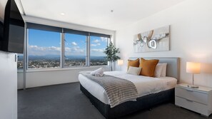 A modern hotel room with a large bed, a TV, a nightstand, a lamp, and a view of the city.