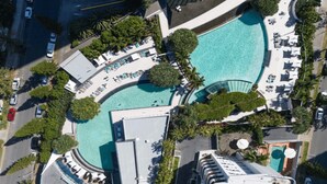 An aerial view of a resort with a large pool, multiple lounge areas, and surrounding greenery.