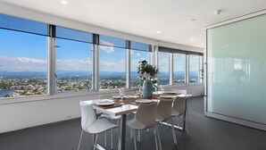 A modern office space with a large table set for dining, large windows offering a city view, and a glass partition wall.