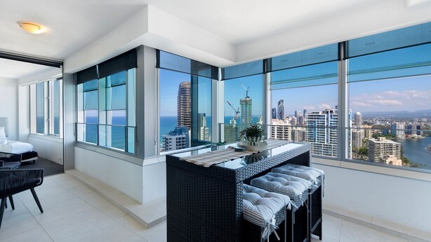 A modern hotel room with large windows, a bed, a seating area, and a view of the city skyline.