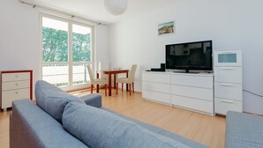 A modern living room with a sofa, a dining table with chairs, a TV, and a white cabinet. - ShortStayPoland Św. Wincentego B7 (Warsaw)