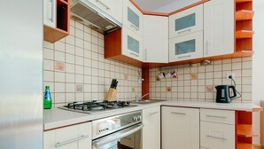 A compact kitchen with white cabinets, a gas stove, a built-in oven, and a kettle. - ShortStayPoland Św. Wincentego B7 (Warsaw)