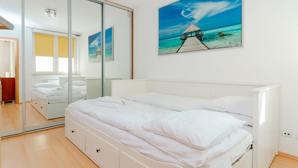 A bedroom with a bed, a large mirror, and a painting of a beach scene. - ShortStayPoland Św. Wincentego B7 (Warsaw)
