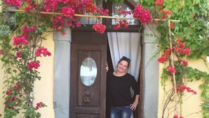 A doorway with a wooden door, a potted plant on either side, and a person standing in the doorway.
