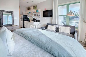 A modern hotel room with a large bed, a sofa, a dining area, and a TV.