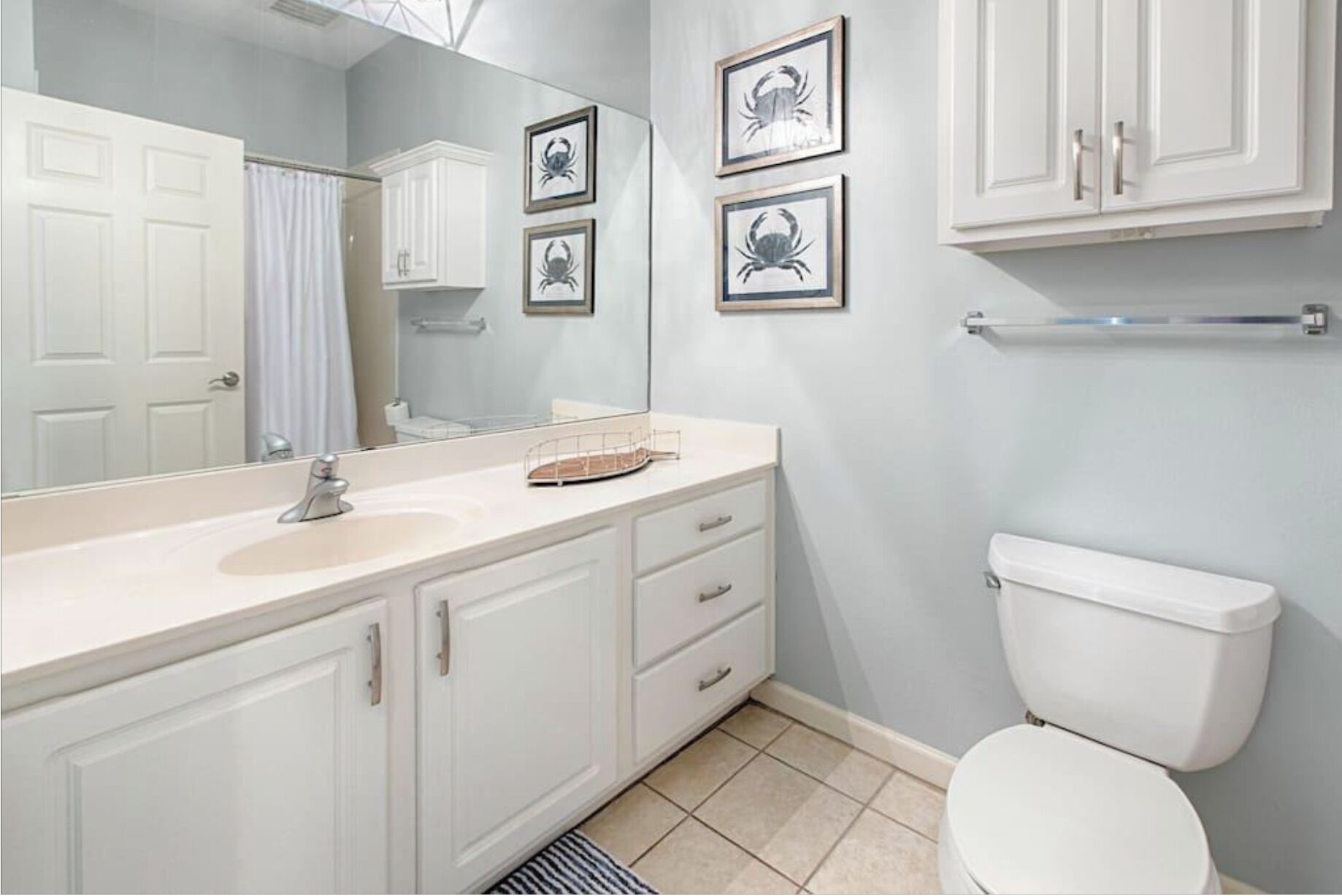 Une salle de bain avec un lavabo blanc, un miroir, des placards, des toilettes et des tableaux encadrés accrochés au mur.