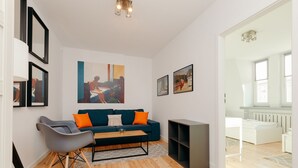 Un salon moderne avec un canapé bleu, des fauteuils gris et une table basse. Les murs sont ornés d’œuvres d’art encadrées, et une grande fenêtre laisse entrer la lumière naturelle.