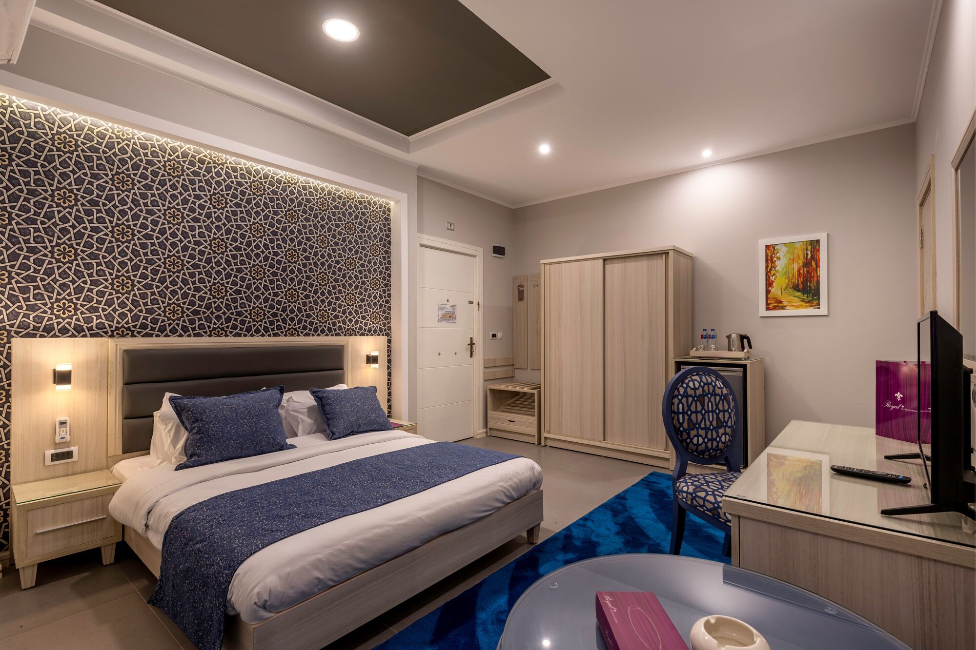 A modern hotel room with a large bed, a desk, a wardrobe, and a TV.