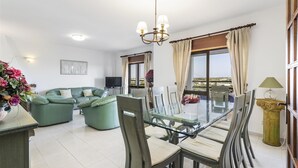 Ein geräumiger Wohnbereich mit einem Glastisch, grünen Sofas und einem Fernseher.