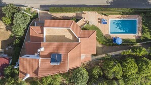 Eine Vogelperspektive auf ein Haus mit einem Ziegeldach, einem Schwimmbecken und einer Terrassenanlage.