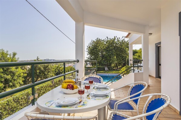A balcony with a table set for two, a pool, and a view of greenery. - Casa Moura, A/C, wi-fi, private pool, barbecue (Vilamoura)