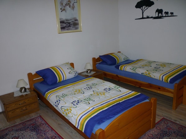 A bedroom with two wooden beds, each with a blue and white bedspread, a bedside table with a lamp, and a nightstand. - Gasthaus - Pension Am Buchberg (Mönchsdeggingen)