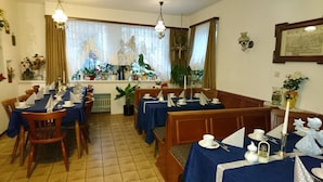 A dining area with tables set for a meal, featuring blue tablecloths, wooden chairs, and a variety of tableware. - Gasthaus - Pension Am Buchberg (Mönchsdeggingen)