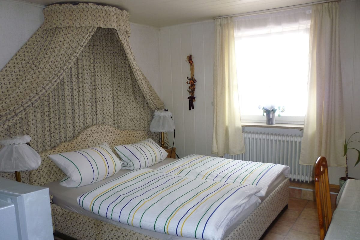 A neatly made bed with striped bedding, a bedside lamp, and a window with curtains.