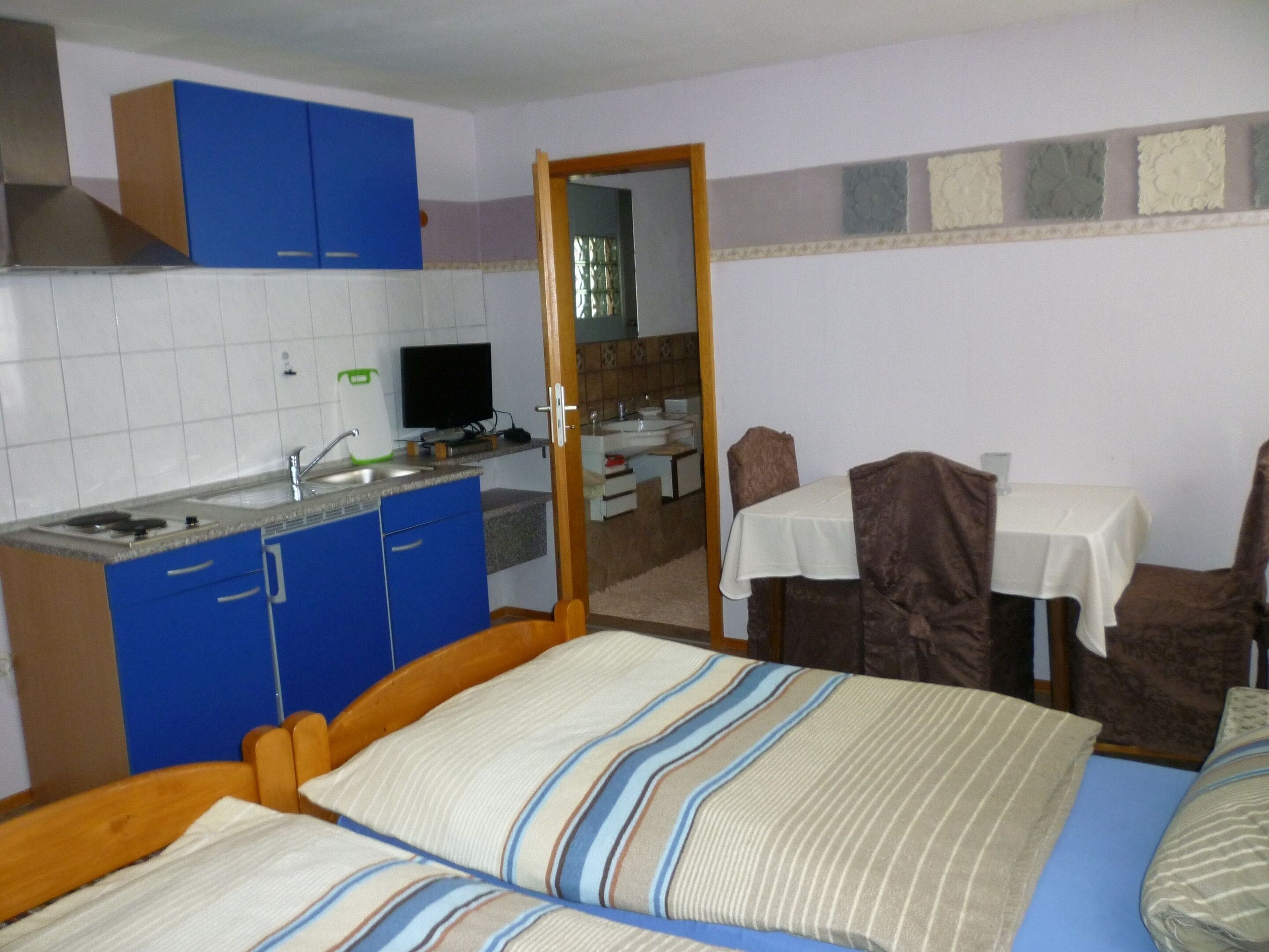 A compact room with a bed, a small kitchenette, a dining table, and a mirror.