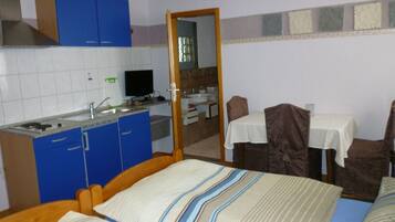 A compact room with a bed, a small kitchenette, a dining table, and a mirror.