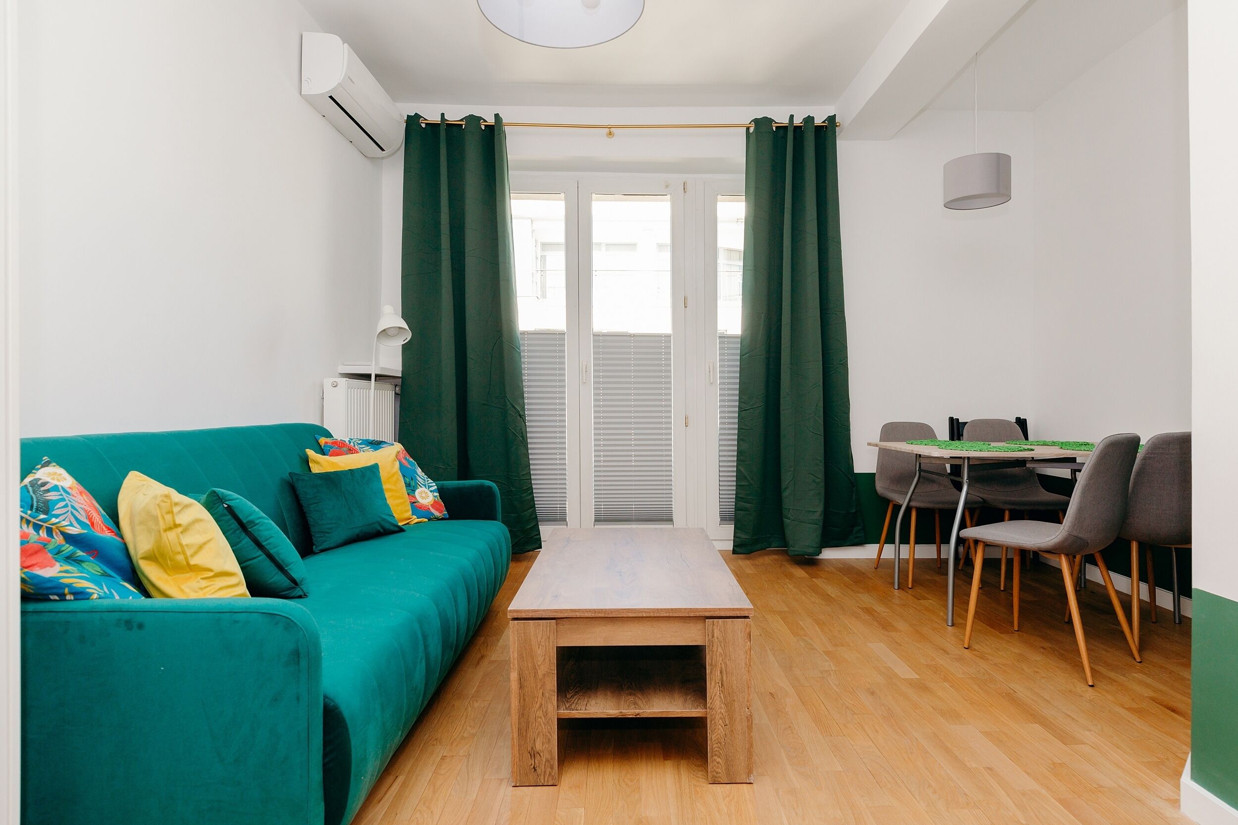 A compact living space with a teal sofa, a wooden coffee table, and a dining area with chairs.