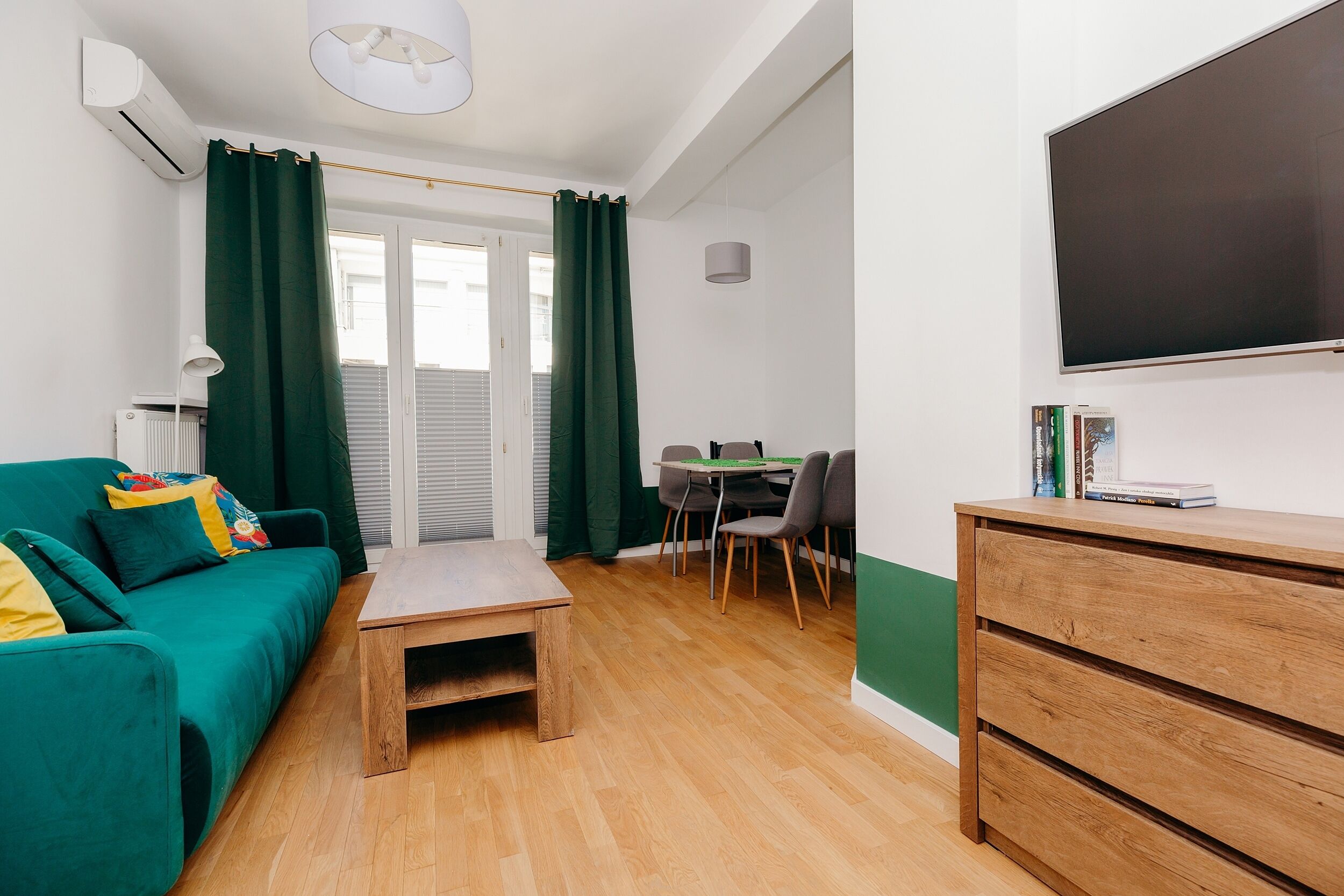 Una sala de estar moderna con un sofá verde, una mesa de centro de madera y un comedor con una mesa y sillas.