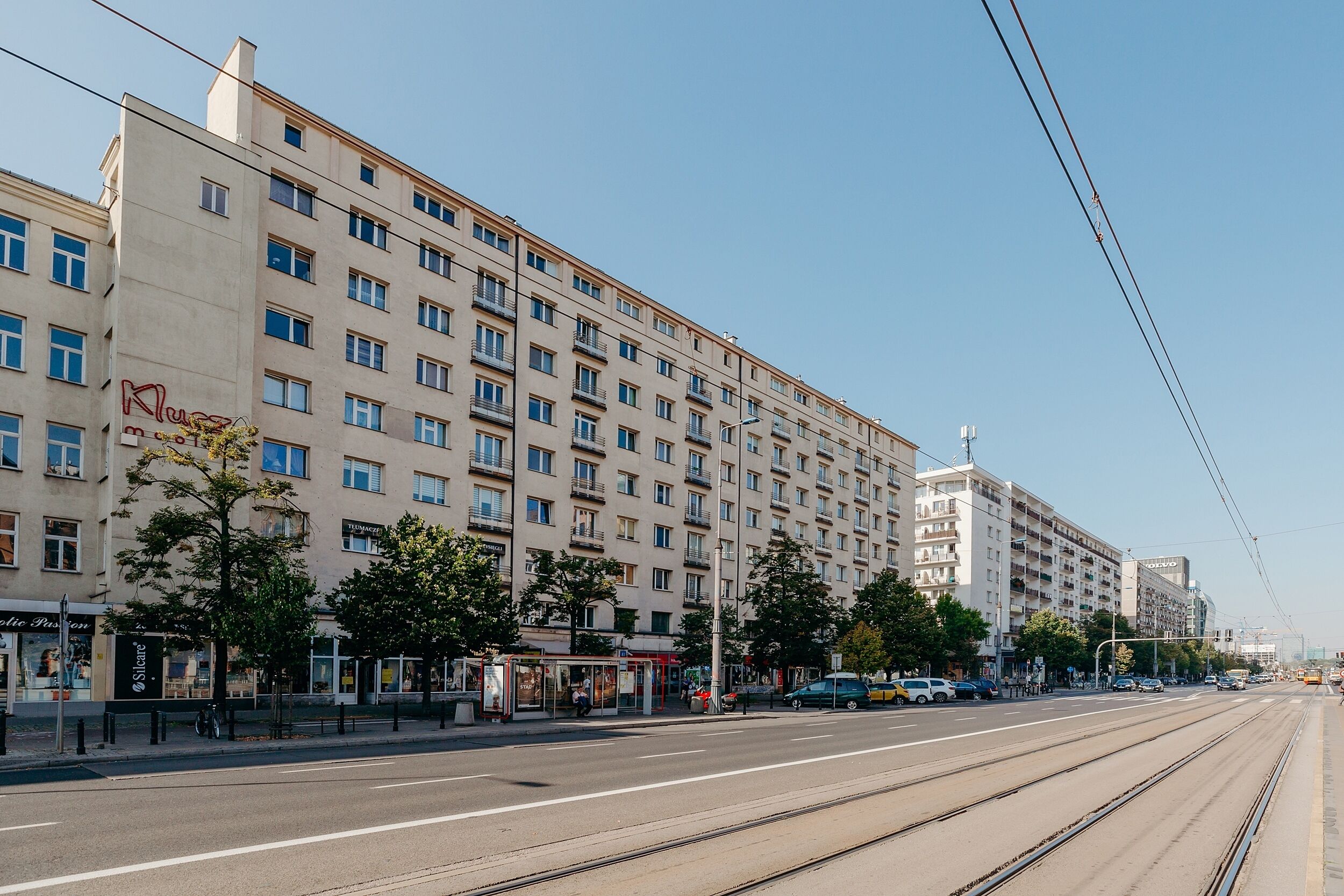 A multi-story hotel with a row of balconies, a tram line, and a pedestrian walkway.