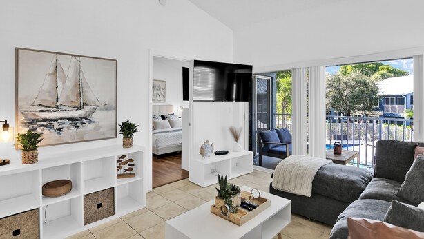 A modern living room with a large sailboat painting, a white entertainment unit, a grey sofa, and a view of the outdoors through large windows. - 280D - Boca Retreat w/ Pool, Parking, Near Evert Tennis & Shops (Boca Raton)