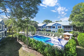 A residential area with a swimming pool surrounded by lush greenery and a blue building with a metal roof. - 280D - Boca Retreat w/ Pool, Parking, Near Evert Tennis & Shops (Boca Raton)