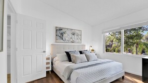 A bedroom with a large bed, a nightstand, a wall-mounted abstract painting, and a window with a view of trees. - 280D - Boca Retreat w/ Pool, Parking, Near Evert Tennis & Shops (Boca Raton)