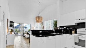 A modern kitchen with white cabinetry, a black countertop, and a built-in oven. There is a hanging light fixture above the sink and a potted plant on the counter. - 280D - Boca Retreat w/ Pool, Parking, Near Evert Tennis & Shops (Boca Raton)