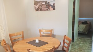 Ein Essbereich mit einem runden Holztisch und vier Stühlen, jeder mit gepolstertem Sitz. Über dem Tisch hängt ein Gemälde einer Küstenlandschaft.