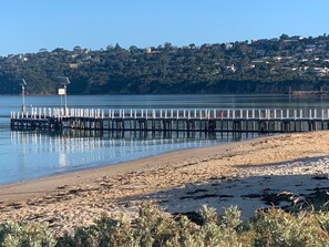 A beach with a wooden pier extending into calm waters, surrounded by greenery and houses in the background. - Cabin in Dromana Holiday Village - Sleeps 7 (Dromana)
