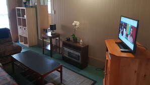 Ein Wohnzimmer mit Fernseher, einem Holzschrank, einem kleinen Tisch und einer Couch.