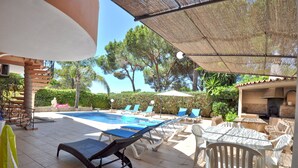 Un espace piscine agrémenté de chaises longues et d’une table, entouré de verdure et surmonté d’une pergola.
