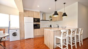 Une cuisine moderne équipée d’un four, d’un micro-ondes et d’un réfrigérateur encastrés. On y trouve également un coin repas avec une table et des chaises, ainsi qu’un lave-linge dans un coin.