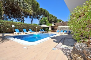 A swimming pool with lounge chairs and umbrellas, surrounded by trees and a building.