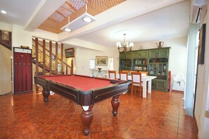 A pool table in a room with a staircase, a dining table, and a green cabinet.