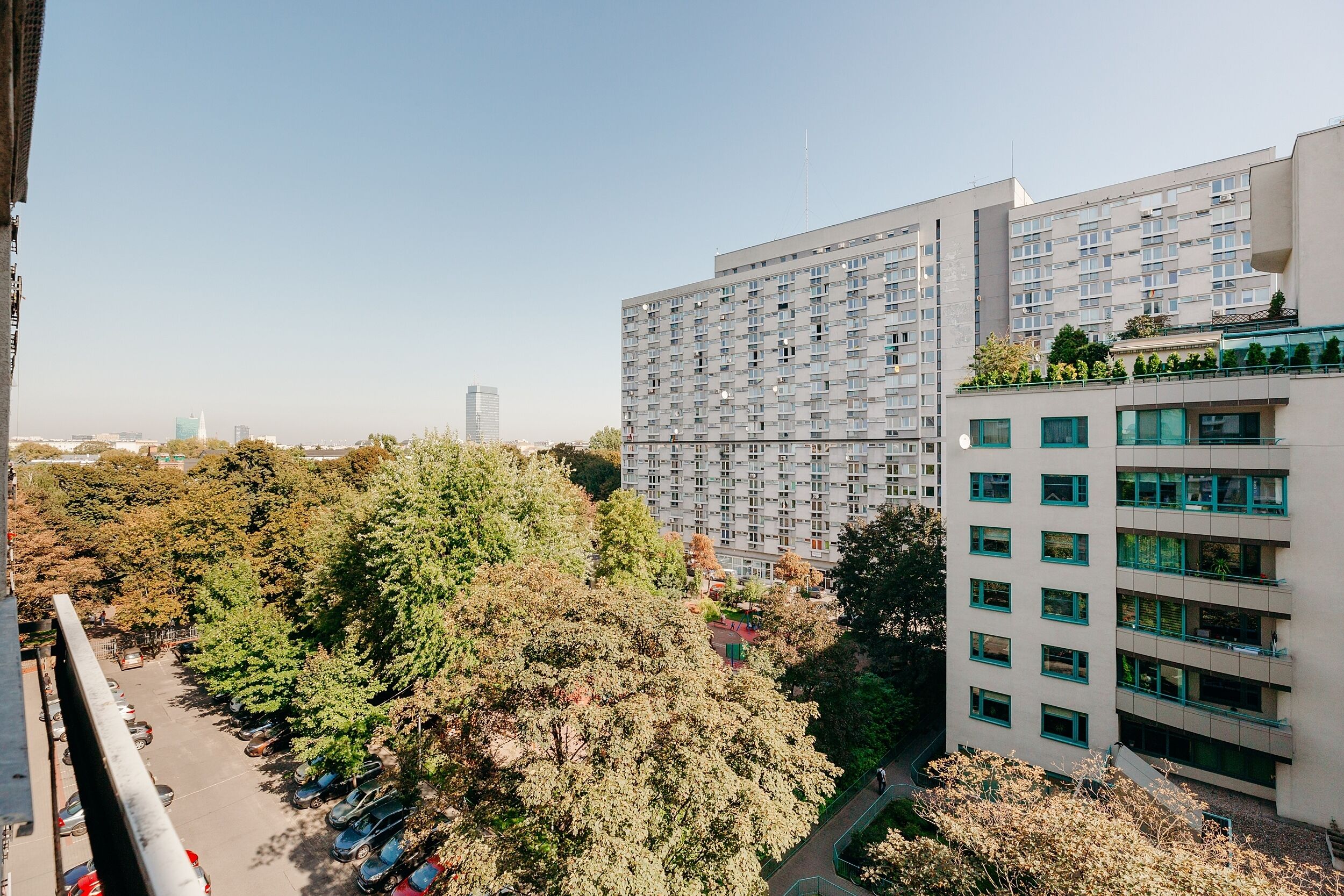 A high-rise building with multiple floors, surrounded by trees and parked cars.