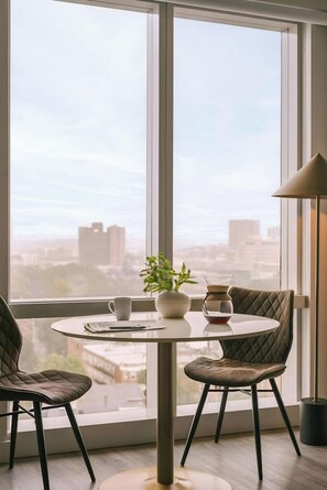 A room with a round table, two chairs, a potted plant, a coffee pot, and a lamp.